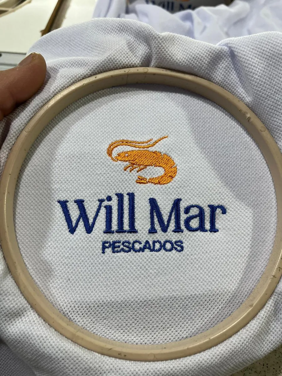 Logo de empresa bordada em camisa polo branca, ainda no bastidor